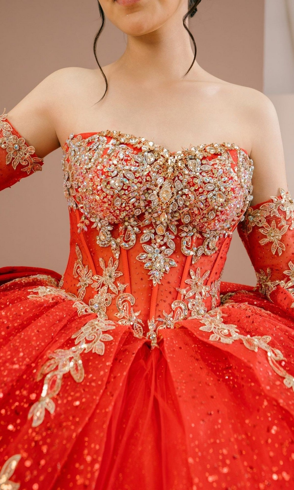 A woman in the Quinceanera Dress 8575JQ by Cinderella Couture, a red, strapless ball gown adorned with gold floral embellishments and matching off-the-shoulder sleeves.